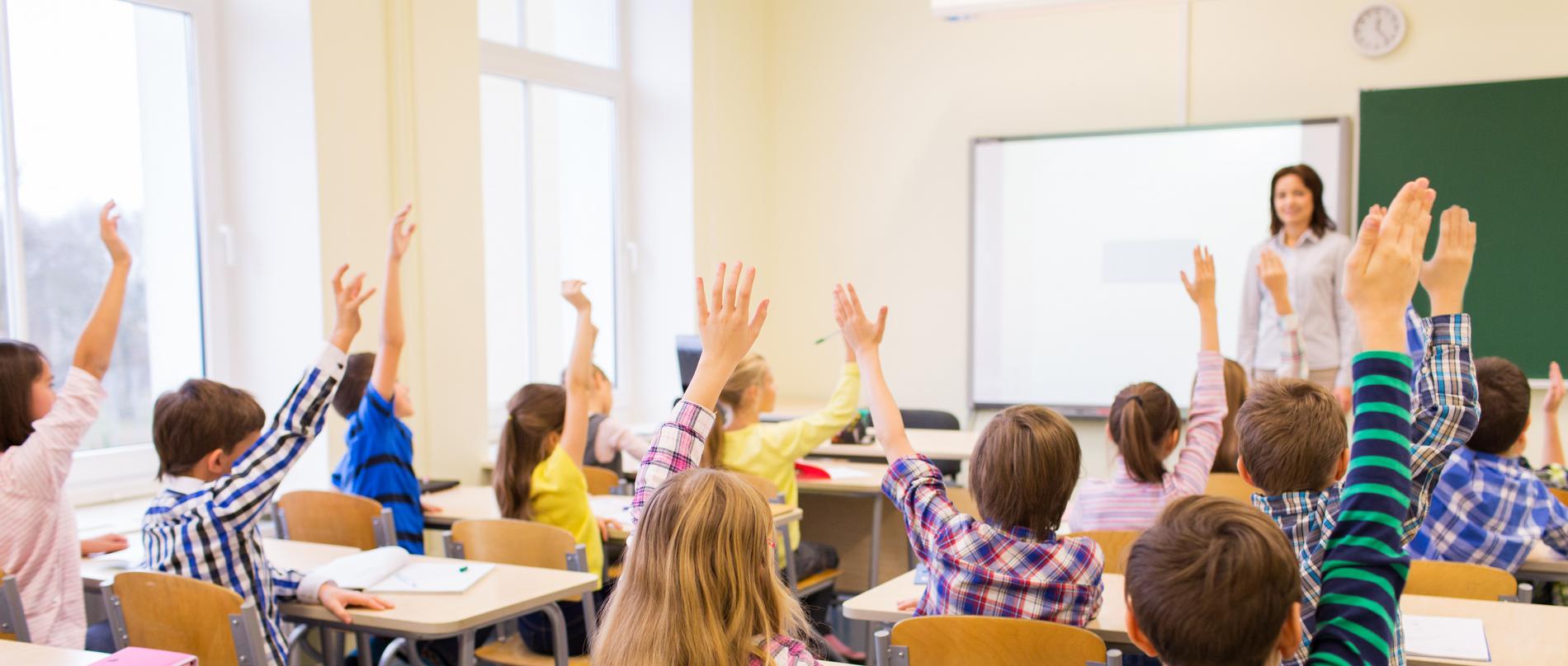 children in classroom raising their hands
